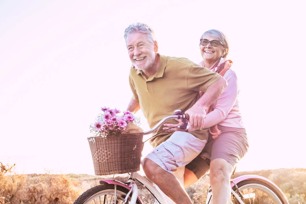 Happy Senior Couple Riding a Bicycle with Flowers Outdoors